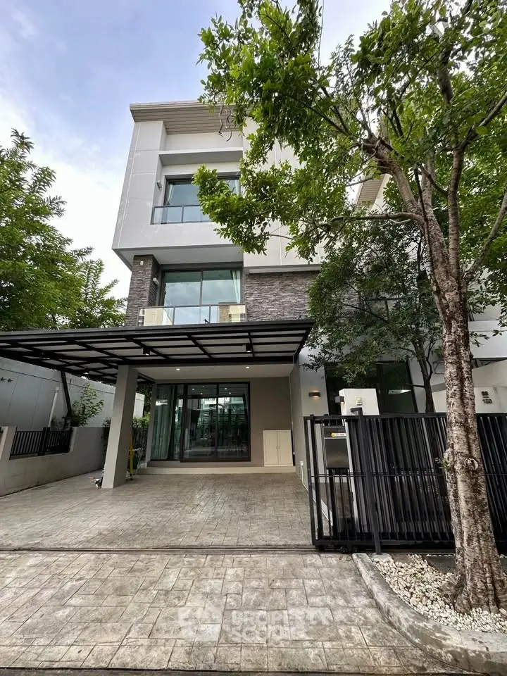 Modern three-story house with sleek design and spacious driveway in a lush green setting.