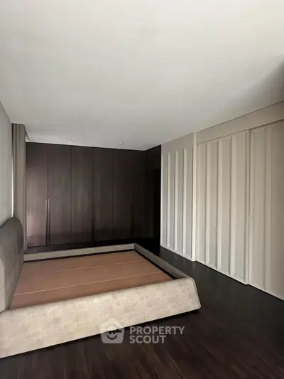 Spacious bedroom with modern design and elegant dark wood flooring.