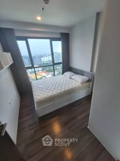 Modern bedroom with large window offering stunning city views, featuring a comfortable bed and sleek wooden flooring.