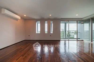 Spacious modern living room with hardwood floors and large windows offering natural light.