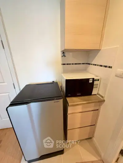 Compact kitchen corner with fridge and microwave in modern apartment.