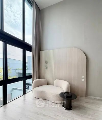 Modern living room with high ceilings and large windows, featuring stylish furniture and natural light.