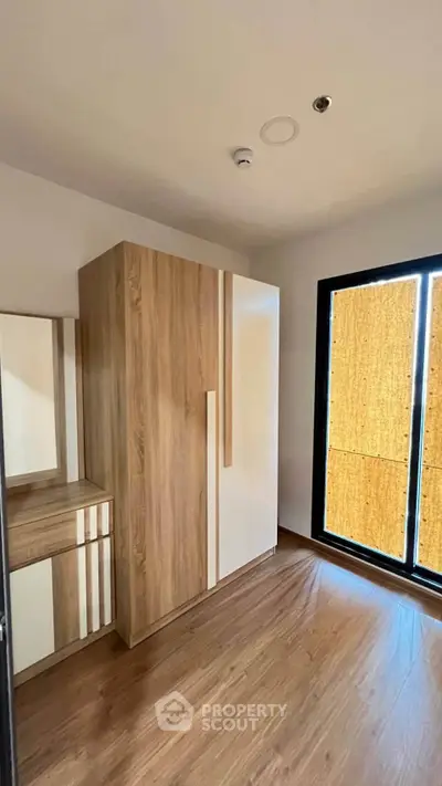 Modern bedroom with wooden flooring and built-in wardrobe, featuring large window for natural light.