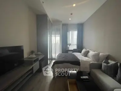 Modern bedroom with cozy bed, stylish sofa, and large TV in a well-lit apartment.