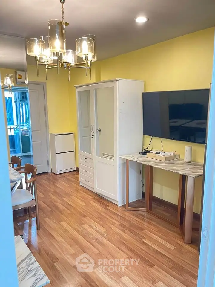 Charming living room with wooden flooring, modern chandelier, and wall-mounted TV for cozy living.