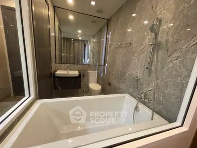 Luxurious bathroom with marble walls and modern fixtures, featuring a spacious bathtub and elegant design.