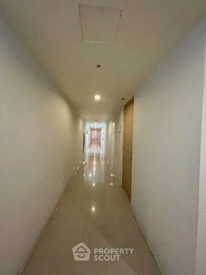 Spacious and well-lit corridor in modern apartment building with sleek tile flooring.