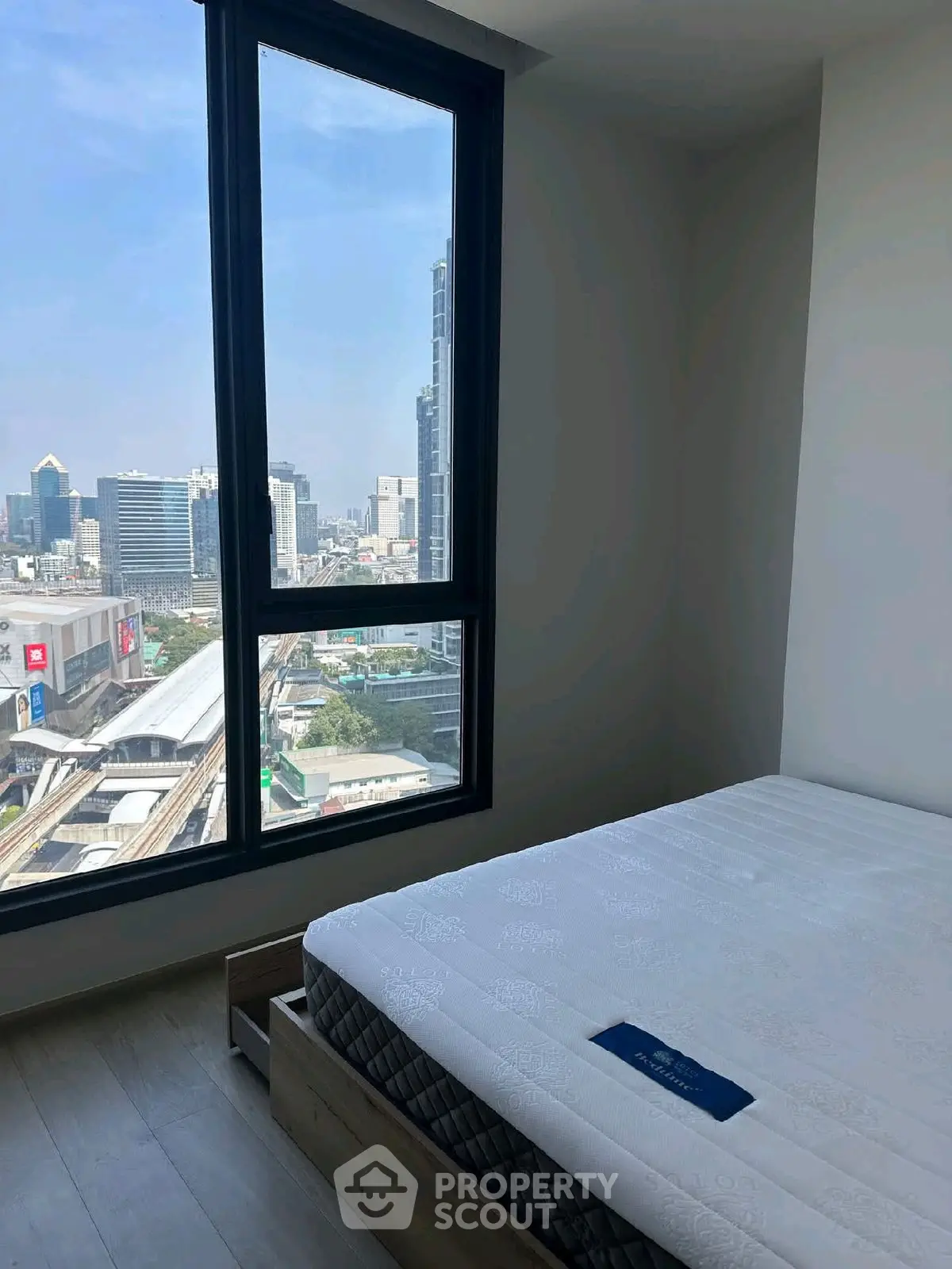 Modern bedroom with city view, featuring large window and comfortable bed in high-rise apartment.