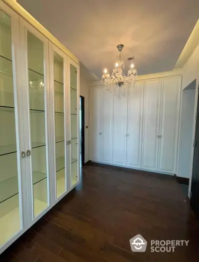 Elegant room with polished hardwood floors and white built-in wardrobes, complemented by a luxurious crystal chandelier, perfect for a sophisticated living space.