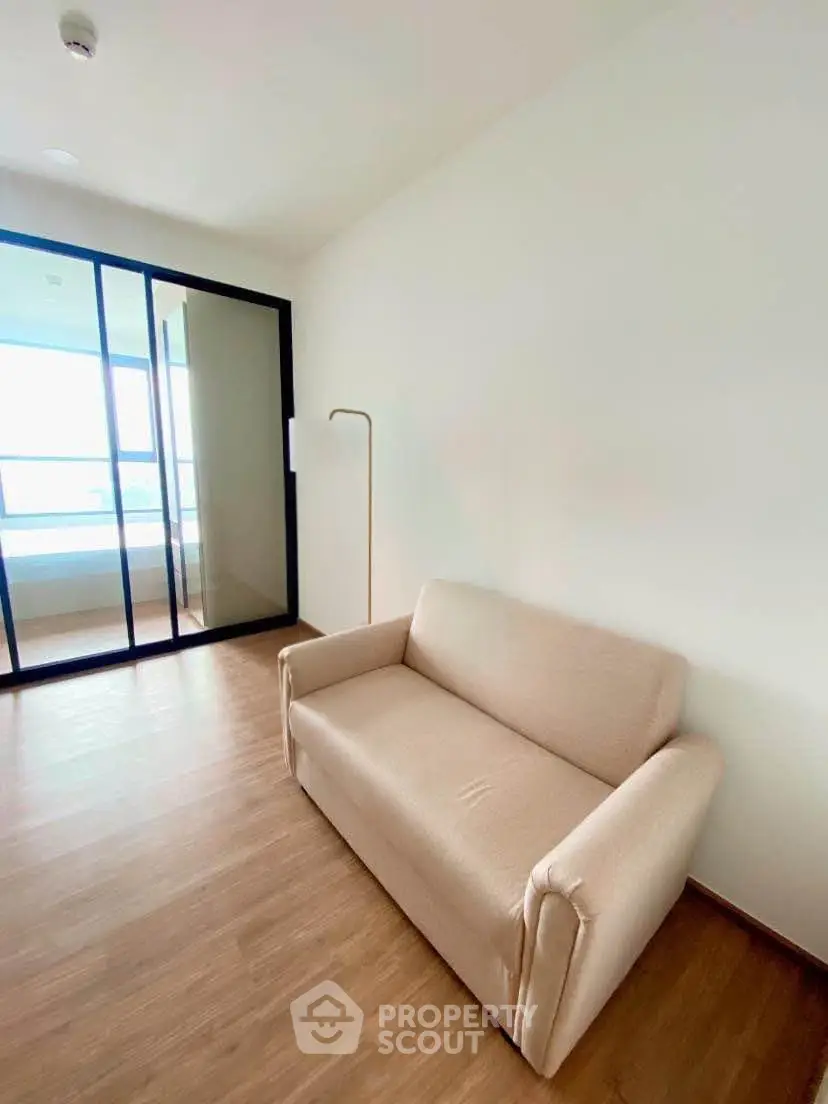 Modern living room with sleek wooden flooring and cozy beige sofa, featuring a glass partition for natural light.