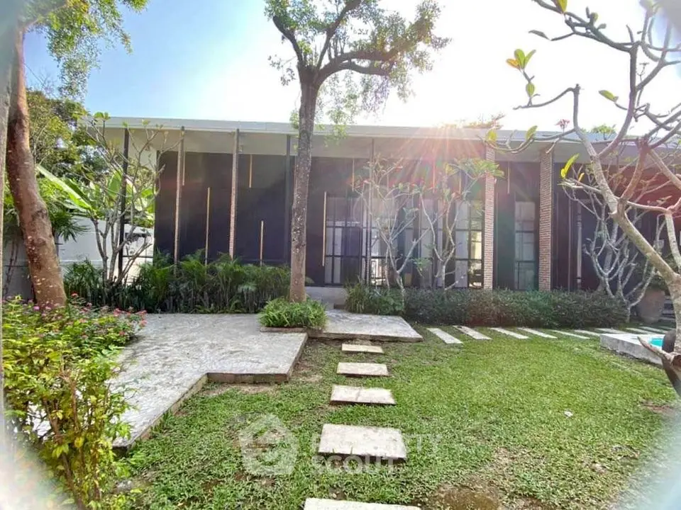 Modern architectural home with lush garden and stone pathway under bright sunlight.