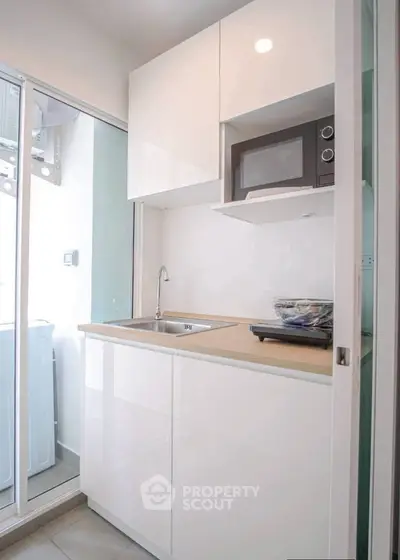 Modern compact kitchen with sleek white cabinets and built-in microwave, featuring a sliding glass door to laundry area.