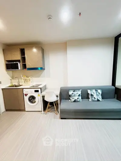 Modern living room with compact kitchen and washing machine, featuring sleek design and cozy seating area.