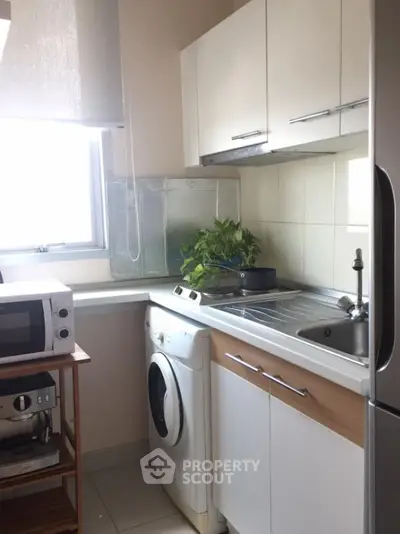 Compact kitchen with washing machine and microwave, ideal for small apartments.