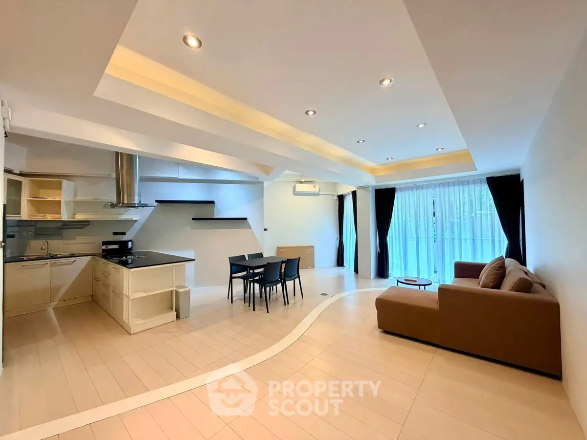 Spacious open-plan living room with modern kitchen and large windows for natural light.