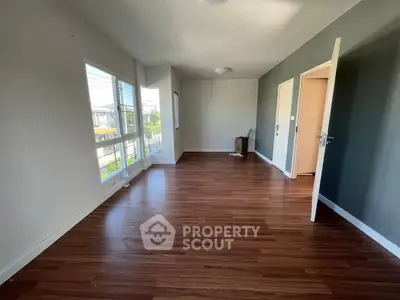 Spacious empty room with wooden flooring and large windows offering natural light.