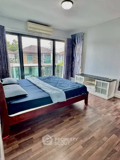 Spacious bedroom with large windows and wooden flooring, offering a cozy and bright atmosphere.