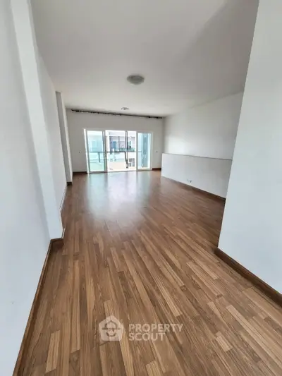 Spacious modern living room with wooden flooring and large windows for natural light.