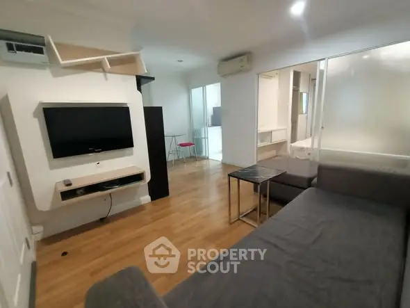 Modern living room with sleek design and wooden flooring, featuring a wall-mounted TV and cozy seating area.