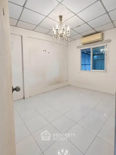 Spacious empty room with chandelier and air conditioning, ideal for customization.