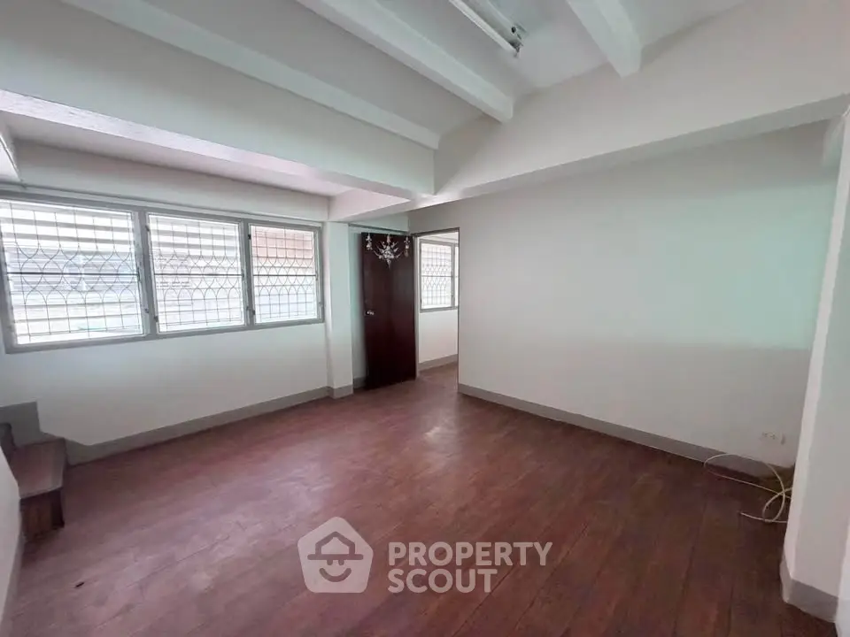 Spacious empty room with wooden flooring and large windows, ideal for customization.