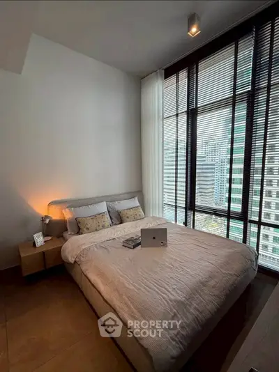 Modern bedroom with large windows offering stunning city views, featuring a cozy bed and stylish decor.