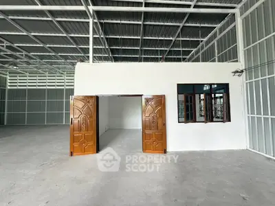 Spacious industrial warehouse with high ceilings and wooden doors, ideal for storage or commercial use.