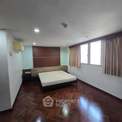 Spacious bedroom with wooden flooring and large window offering natural light.