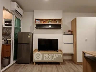 Modern living room with sleek TV setup and stylish shelving, adjacent to a compact kitchen area.