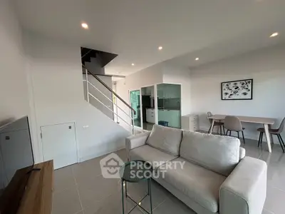Modern living room with sleek furniture and open layout, featuring a staircase and dining area.