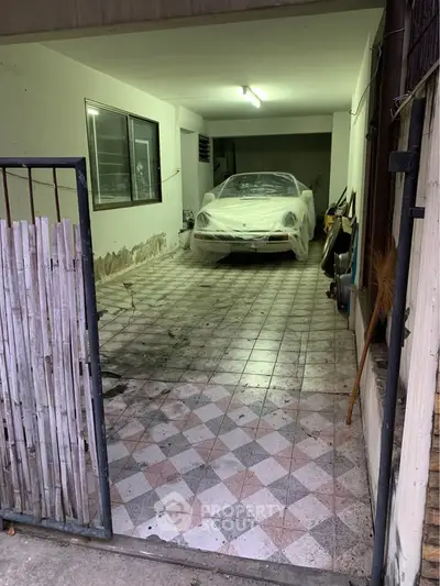 Covered car in a tiled garage with gated entrance, ideal for secure parking.