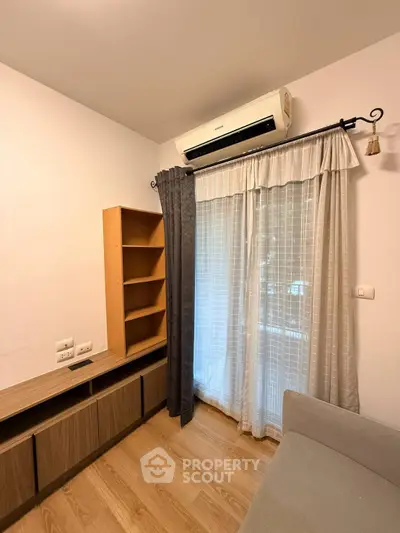 Cozy living room with air conditioning and wooden flooring, featuring a stylish curtain and modern shelving.