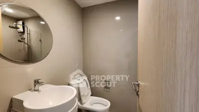 Modern bathroom with sleek fixtures and round mirror, featuring a shower and toilet.