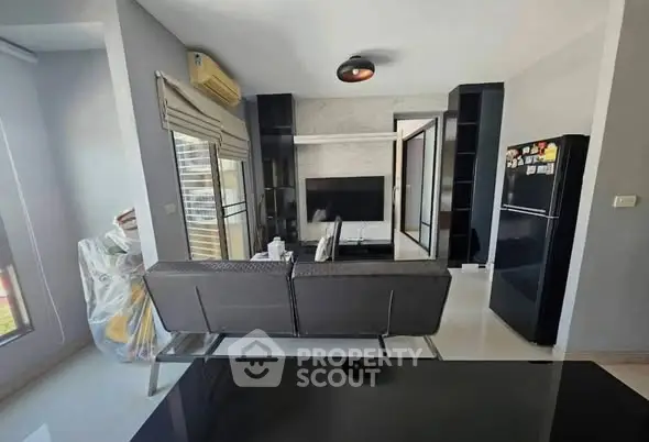 Modern living room with sleek furniture and large TV, featuring a stylish black refrigerator.