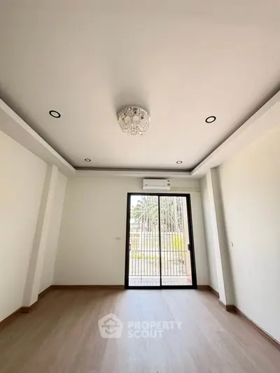 Spacious empty room with elegant ceiling light and large window offering natural light.