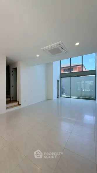 Spacious modern living room with large windows and high ceiling, offering abundant natural light and sleek tile flooring.