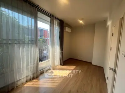 Bright and airy room with wooden flooring and large window overlooking balcony.