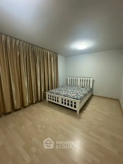 Spacious bedroom with wooden flooring and elegant curtains, featuring a cozy bed.