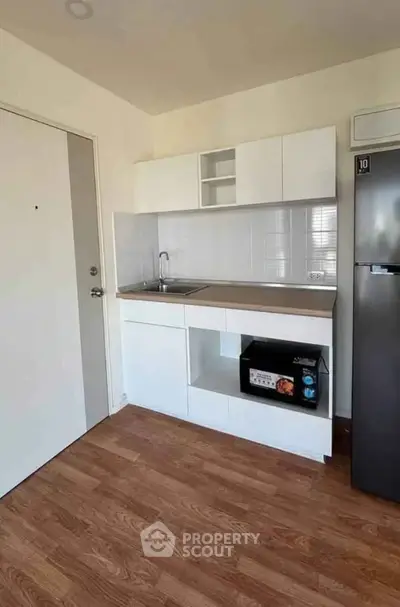 Modern compact kitchen with sleek cabinetry and stainless steel fridge in a cozy apartment.