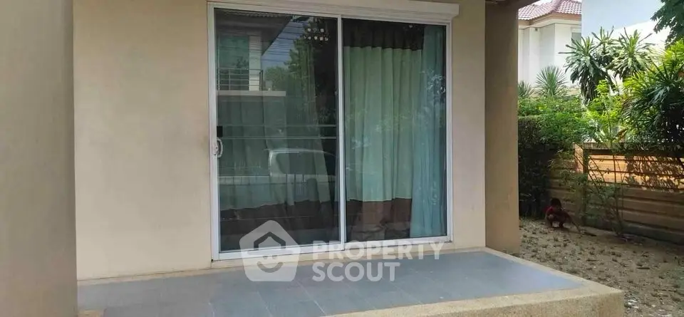 Charming patio with sliding glass doors leading to a cozy interior, surrounded by lush greenery.