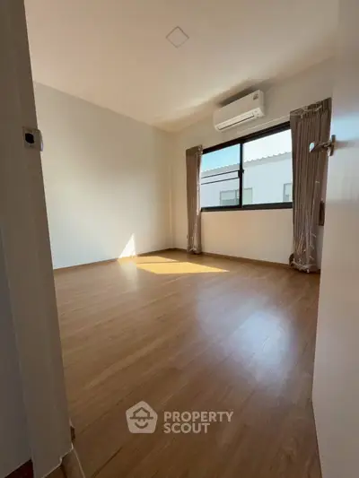 Spacious empty bedroom with wooden flooring and large window, perfect for customization.