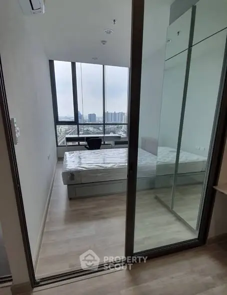 Modern bedroom with floor-to-ceiling windows offering stunning city views, featuring sleek mirrored closet doors.