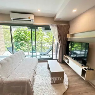 Modern living room with large windows and balcony view, featuring cozy sofa and sleek TV setup.
