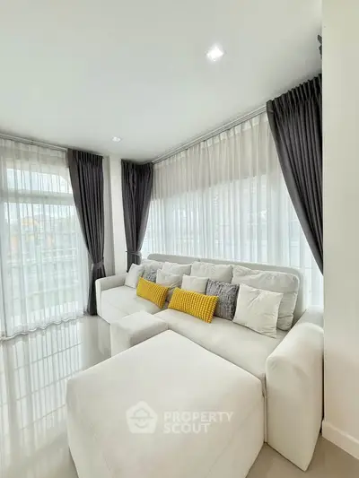 Elegant living room with plush white sofa and floor-to-ceiling windows, perfect for modern living.