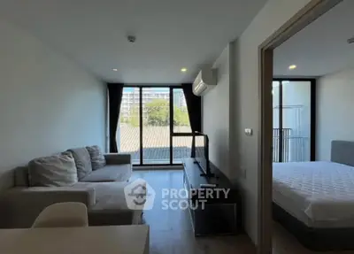 Modern apartment living room with cozy sofa and adjacent bedroom, featuring large windows and natural light.
