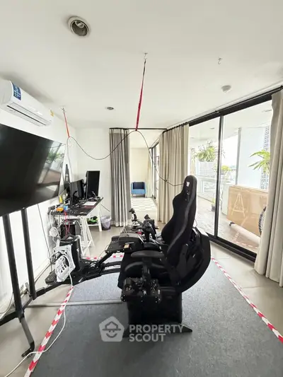 Spacious living room with gaming setup and large balcony access, perfect for entertainment and relaxation.