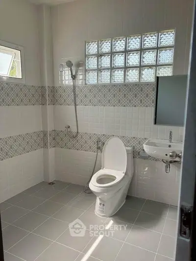 Modern bathroom with sleek tiles and glass block window for natural light.