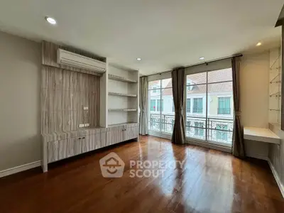 Spacious living room with wooden floors and large windows offering a charming view of neighboring houses.
