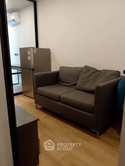 Cozy small living room with a gray sofa and compact fridge, ideal for modern apartments.