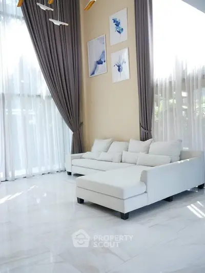 Luxurious living room with high ceilings, elegant curtains, and modern white sofa.